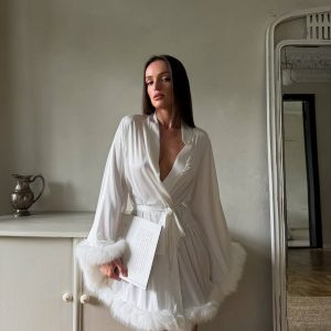 Розкішний білосніжний жіночий халат Snow White з м'яким пухнастим оздобленням, що лежить на ліжку або висить на вішалці, демонструючи текстуру та елегантність. Ідеально для домашнього комфорту.